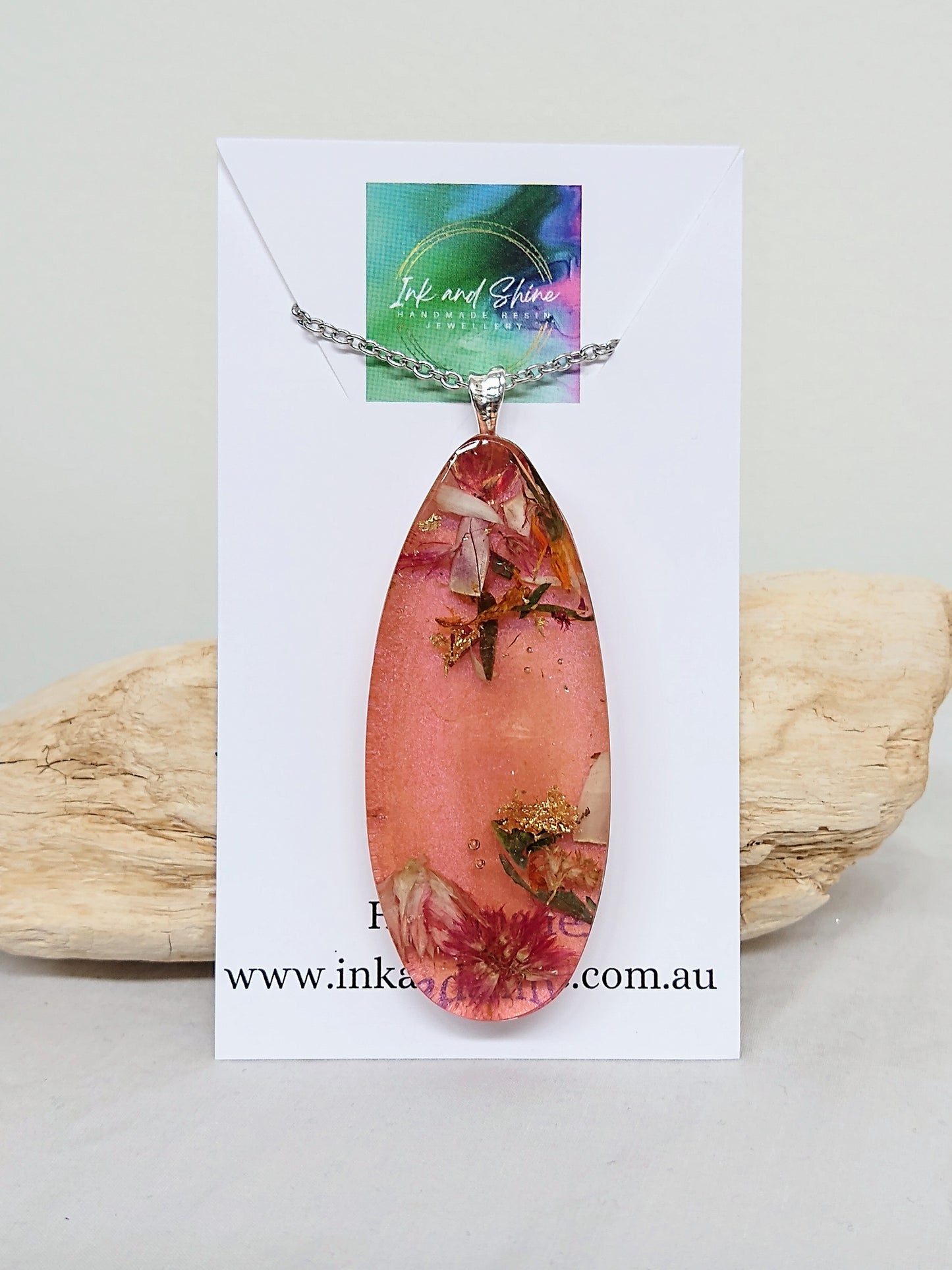 Ellipse shaped resin pendant necklace coloured with orange/pink mica powder and filled with organic dried flowers, on a stainless steel chain.